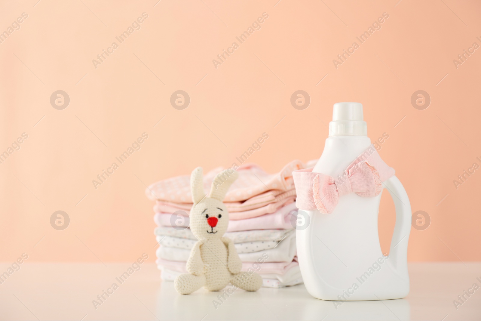 Photo of Detergent, toy and children's clothes on white table near pink wall