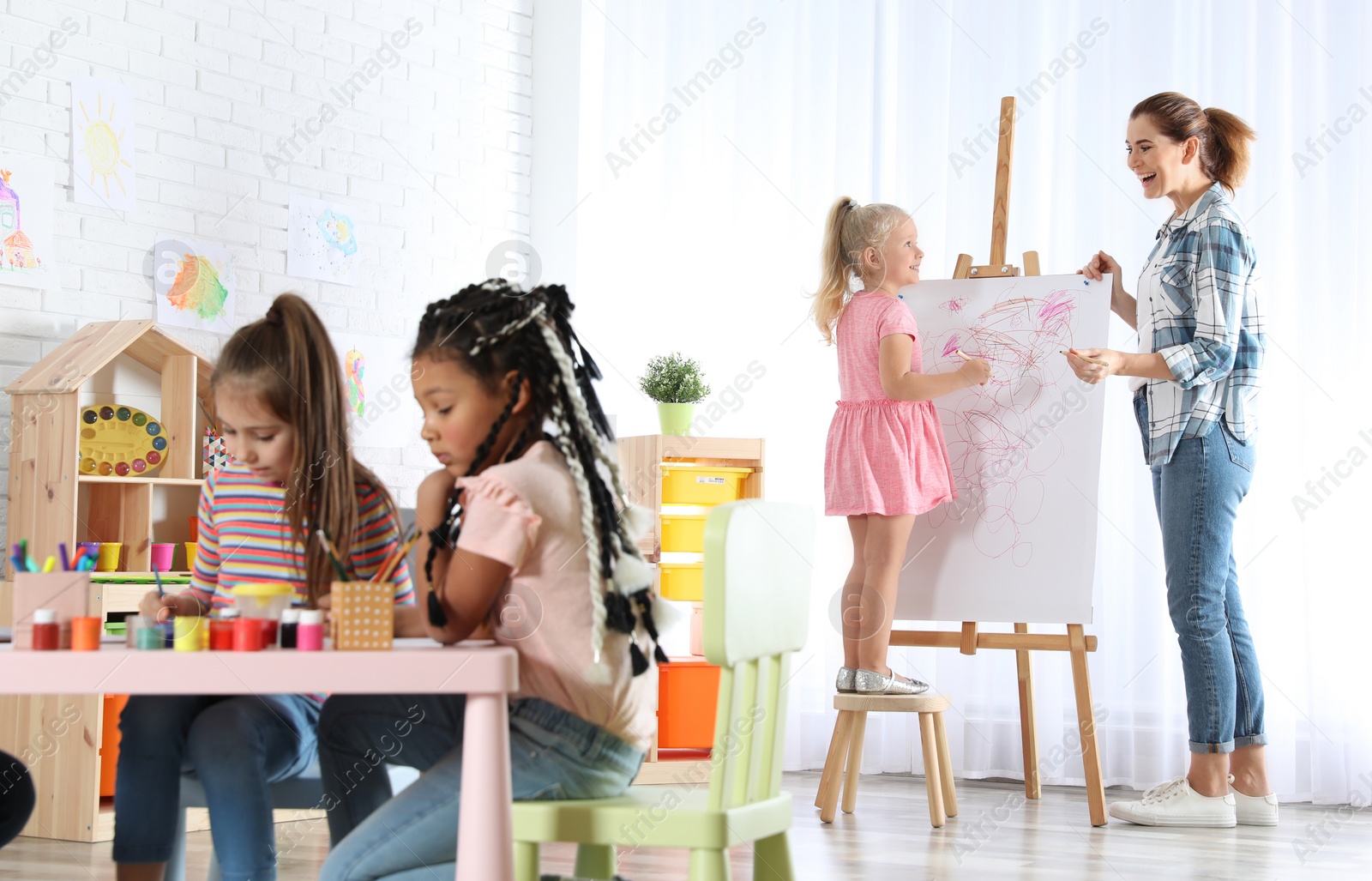 Photo of Female teacher with child near easel at painting lesson indoors