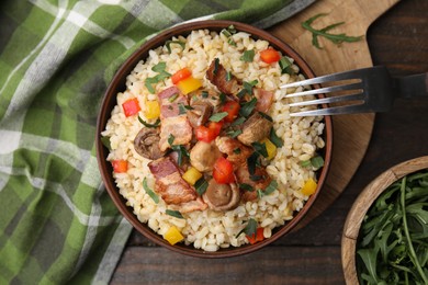 Photo of Cooked bulgur with vegetables, fried bacon and mushrooms in bowl on wooden table, top view