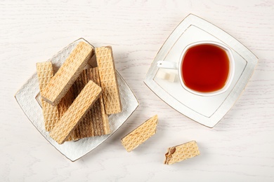 Plate of delicious wafers with cup of tea on white wooden background, top view