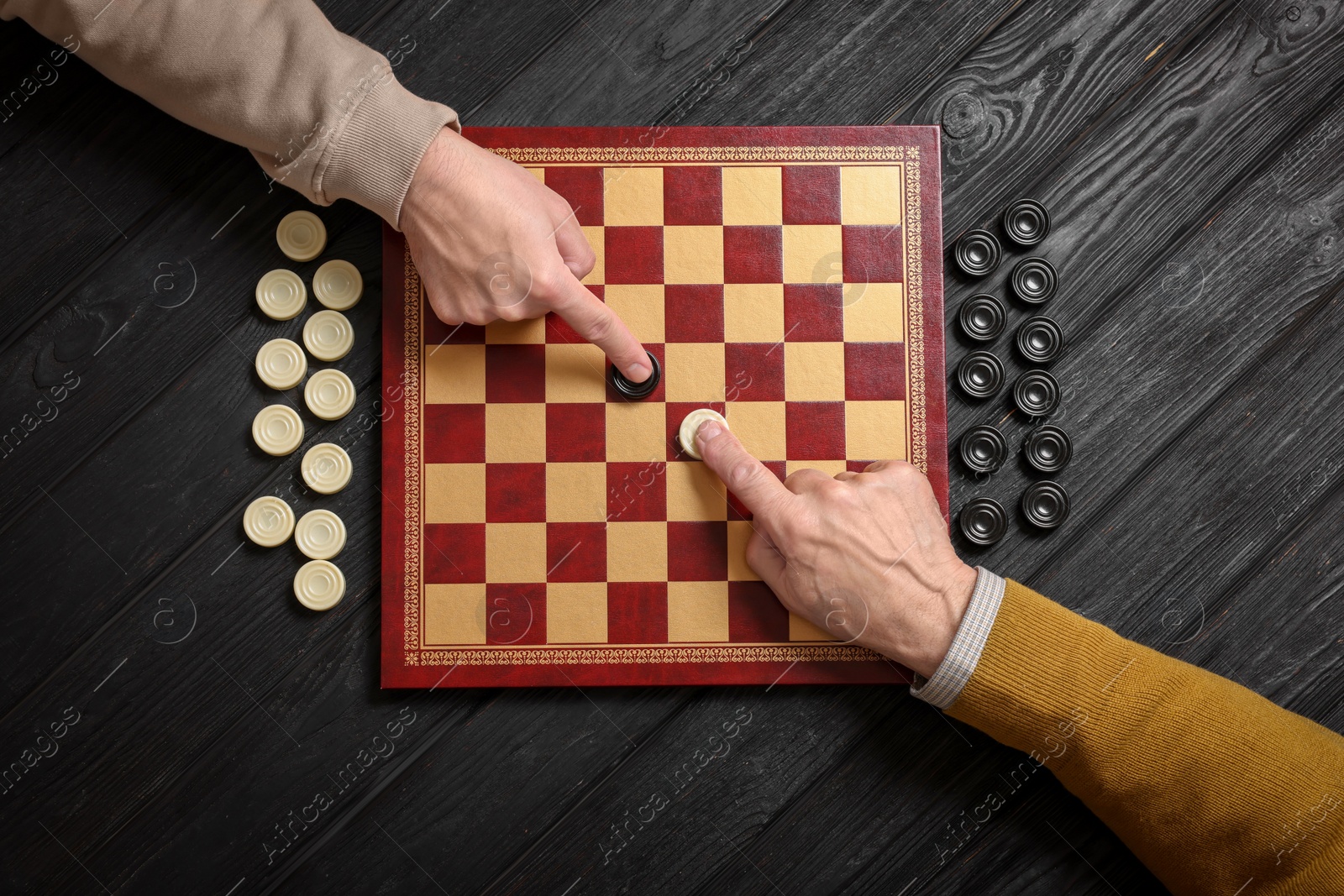 Photo of Man playing checkers with partner at black wooden table, top view