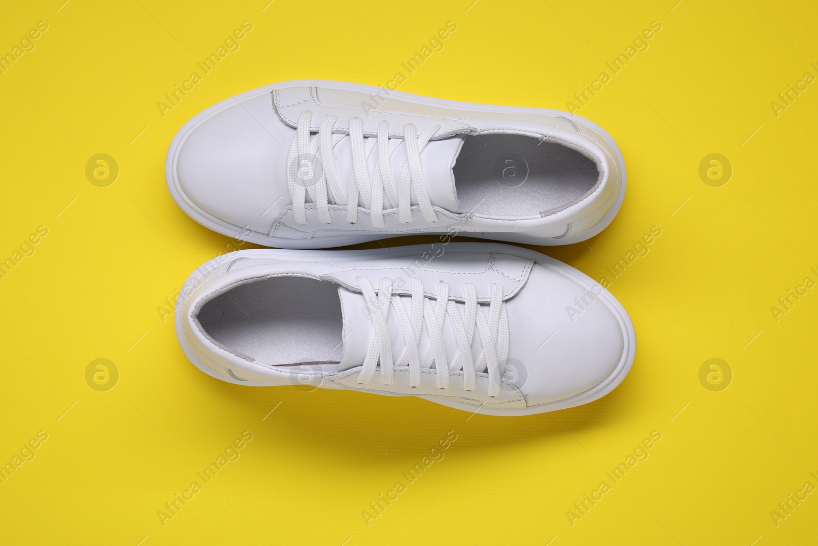 Photo of Pair of stylish white sneakers on yellow background, top view