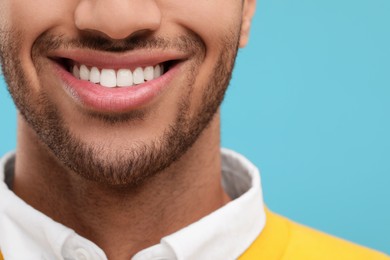 Smiling man with healthy clean teeth on light blue background, closeup