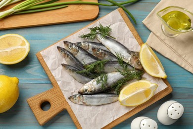 Photo of Fresh raw sprats, dill, oil and cut lemon on light blue wooden table, flat lay