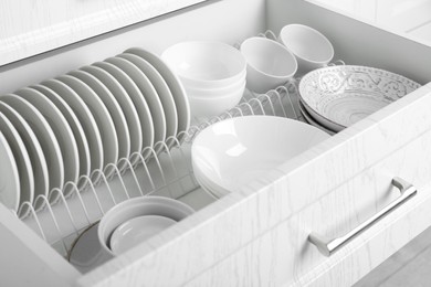 Photo of Open drawer with different plates and bowls in kitchen, closeup