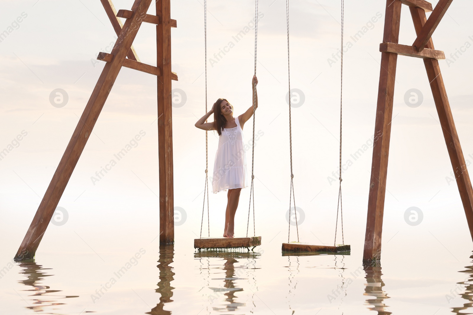 Photo of Young woman enjoying sunrise on swing over water