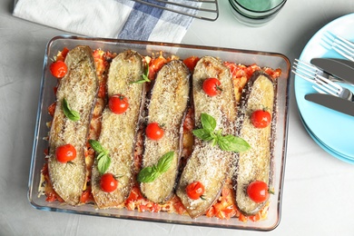 Flat lay composition with baked eggplant, tomatoes and basil in dishware on table