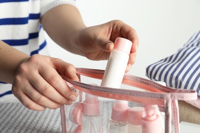 Woman putting small bottle with personal care product into plastic bag, closeup. Cosmetic travel kit