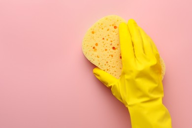 Cleaner in rubber glove holding new yellow sponge on pink background, top view. Space for text