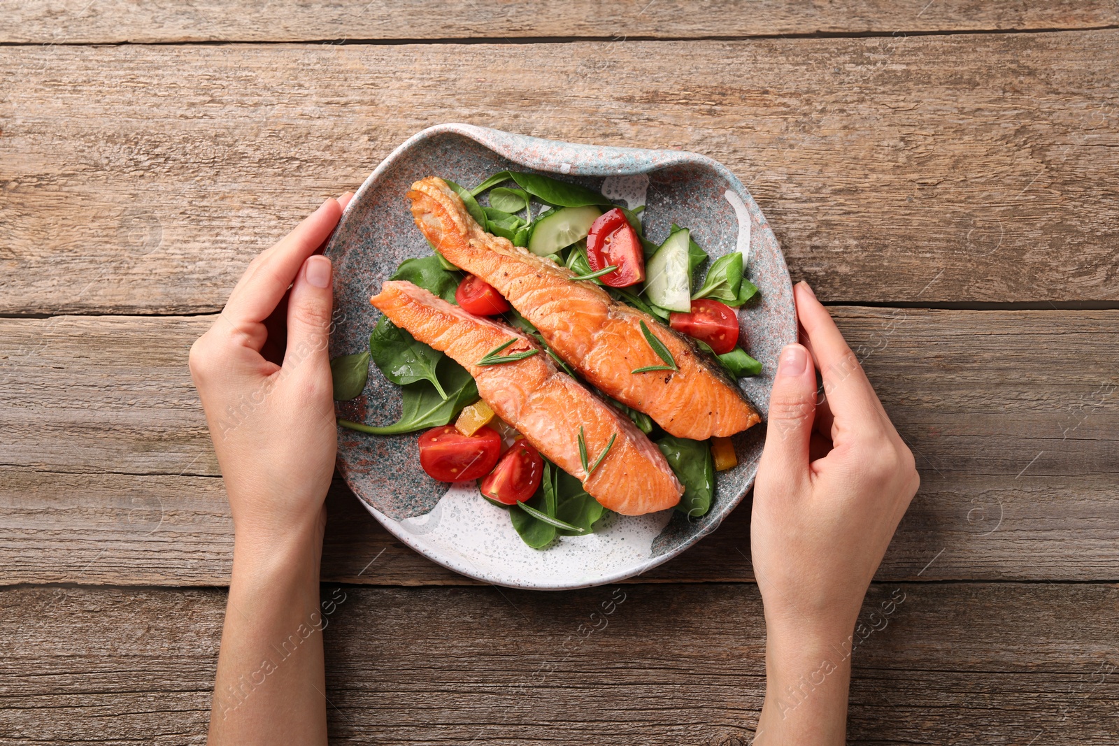 Photo of Healthy meal. Woman with plate of tasty grilled salmon, spinach and vegetables at wooden table, top view