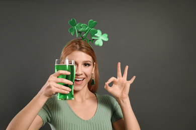 Photo of Young woman with clover headband and green beer on grey background. St. Patrick's Day celebration