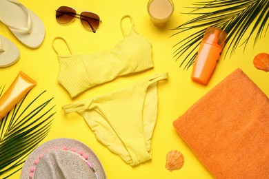 Photo of Beach towel, swimsuit, flip flops, hat. sunglasses and sun protection products on yellow background, flat lay
