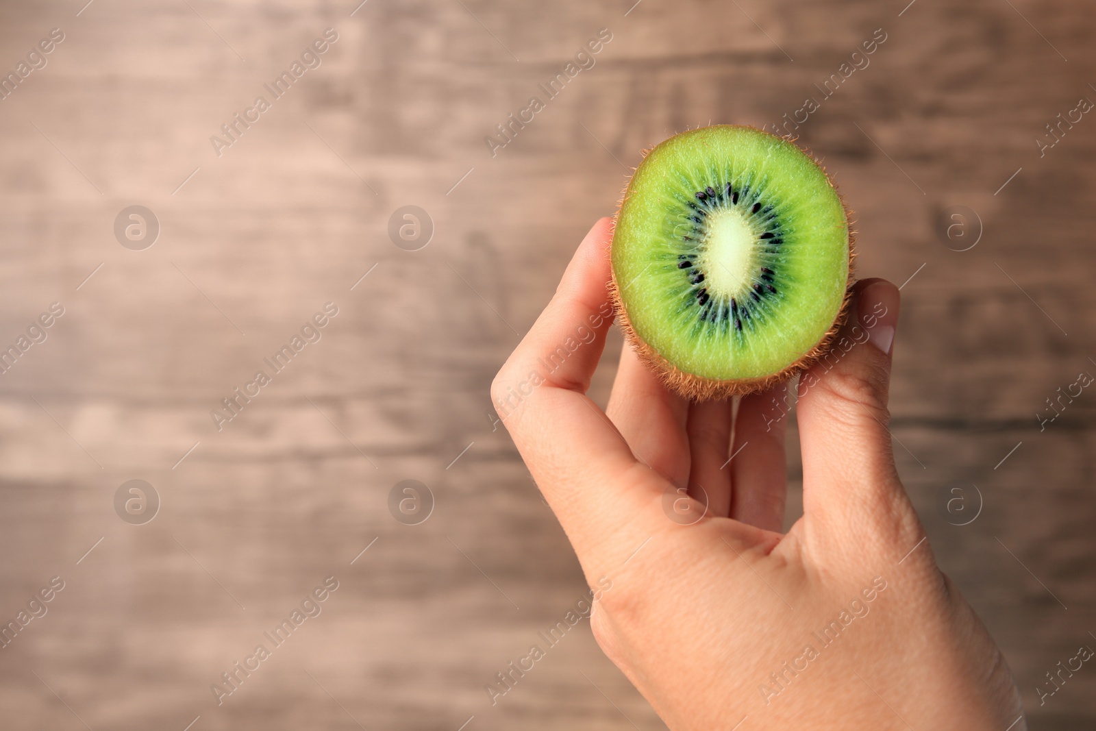 Photo of Woman holding delicious fresh kiwi on wooden background, closeup. Space for text