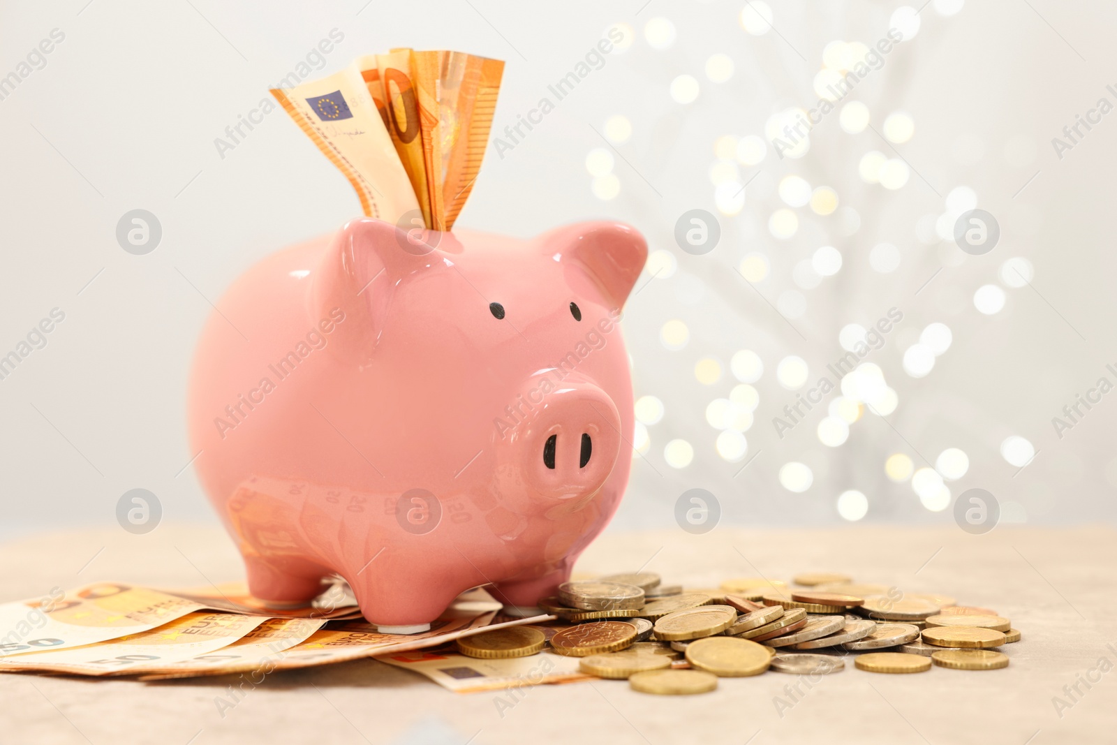 Photo of Piggy bank with euro banknotes and coins on grey table against blurred lights, space for text