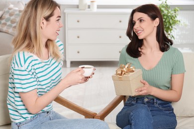 Smiling young woman presenting gift to her friend at home