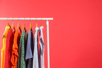 Photo of Bright clothes hanging on rack against red background, space for text. Rainbow colors