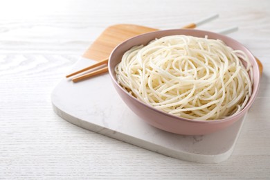 Bowl of tasty cooked rice noodles and chopsticks on white wooden table. Space for text