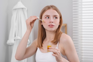 Photo of Woman applying essential oil onto face in bathroom