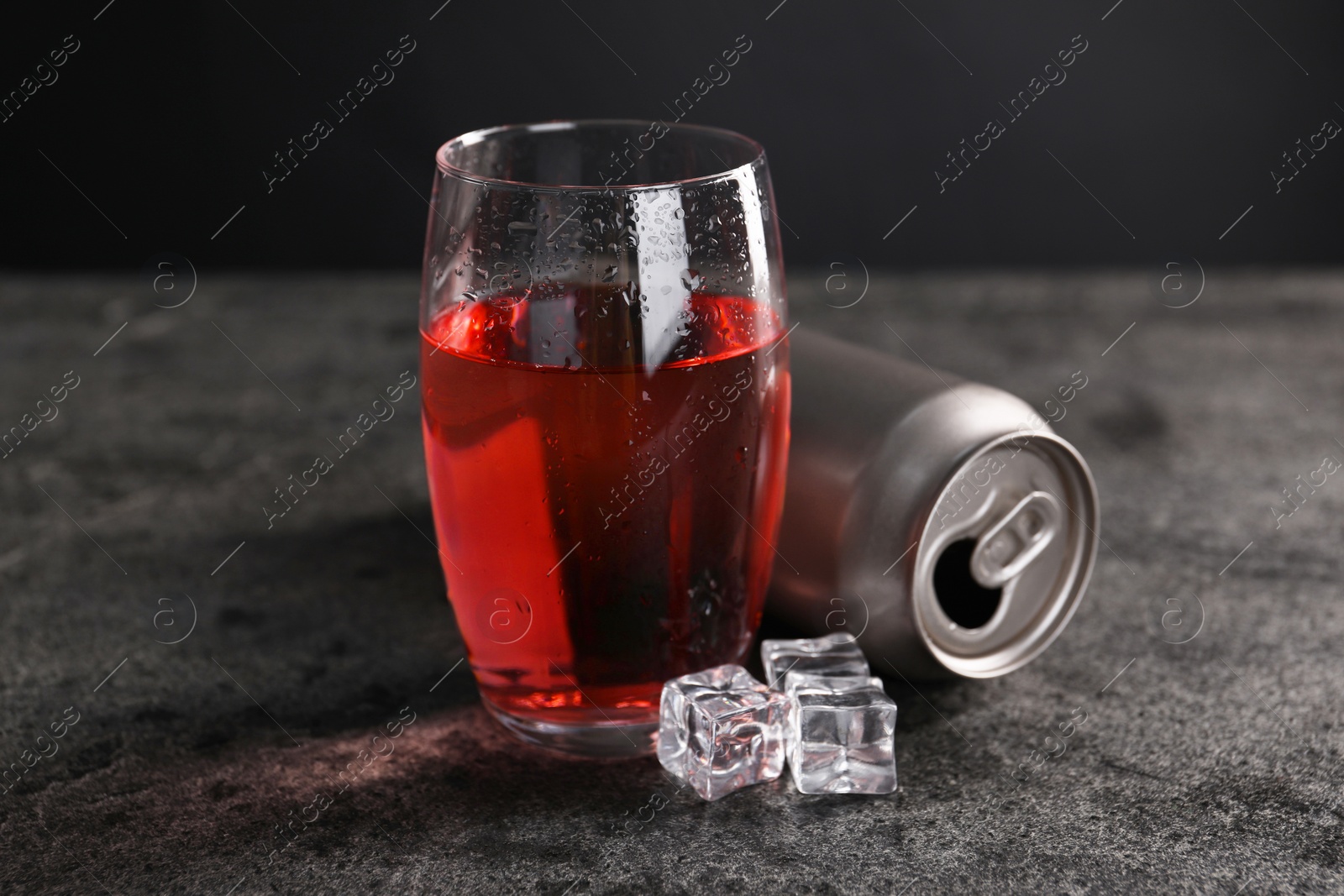 Photo of Energy drink in glass, aluminium can and ice cubes on grey table, closeup