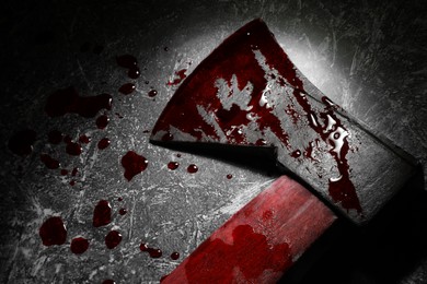 Axe with blood on dark gray textured surface in darkness, top view