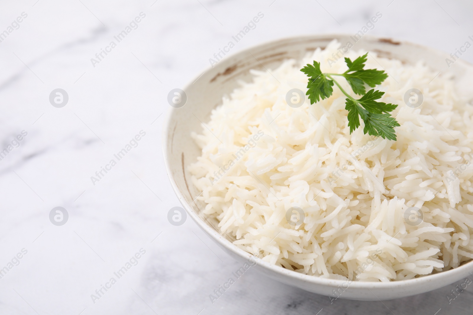 Photo of Bowl of delicious rice with parsley on light table, closeup. Space for text