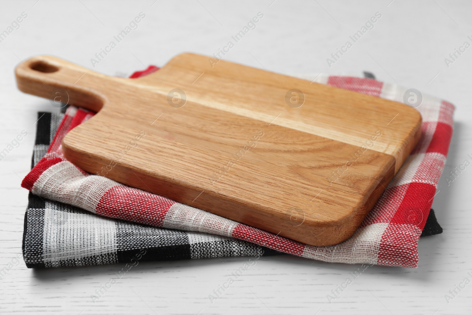 Photo of Wooden board and colorful kitchen towels on white wooden table