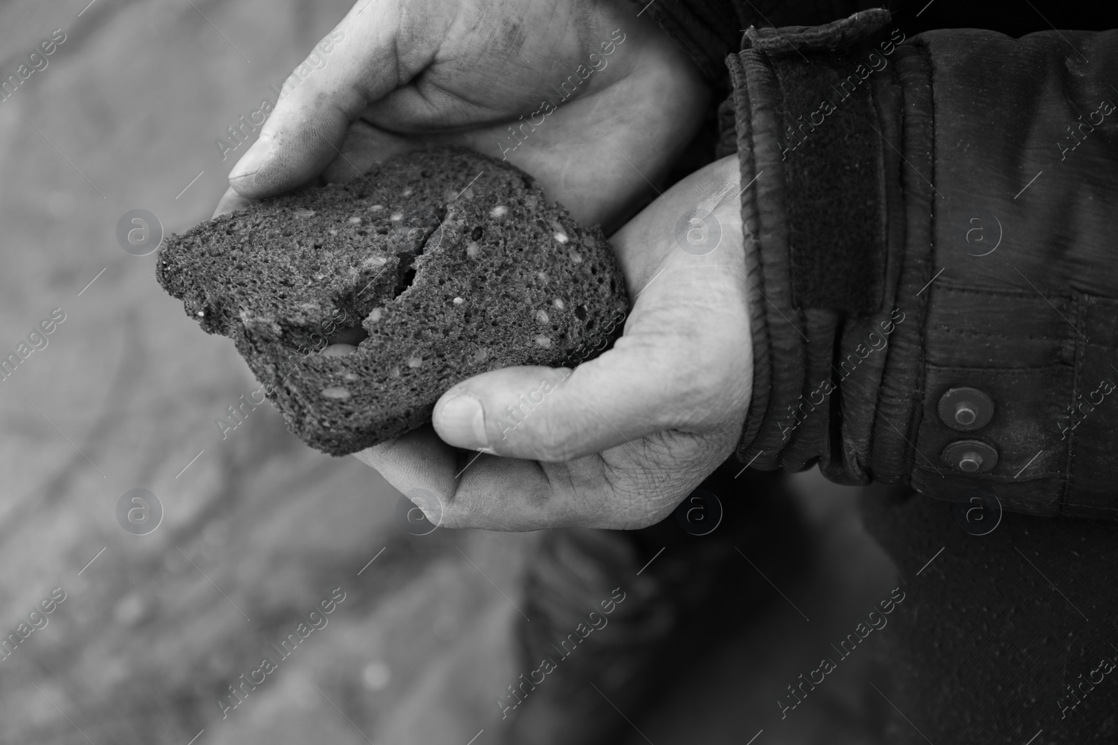 Photo of Poor homeless man holding piece of bread outdoors, closeup. Black and white effect