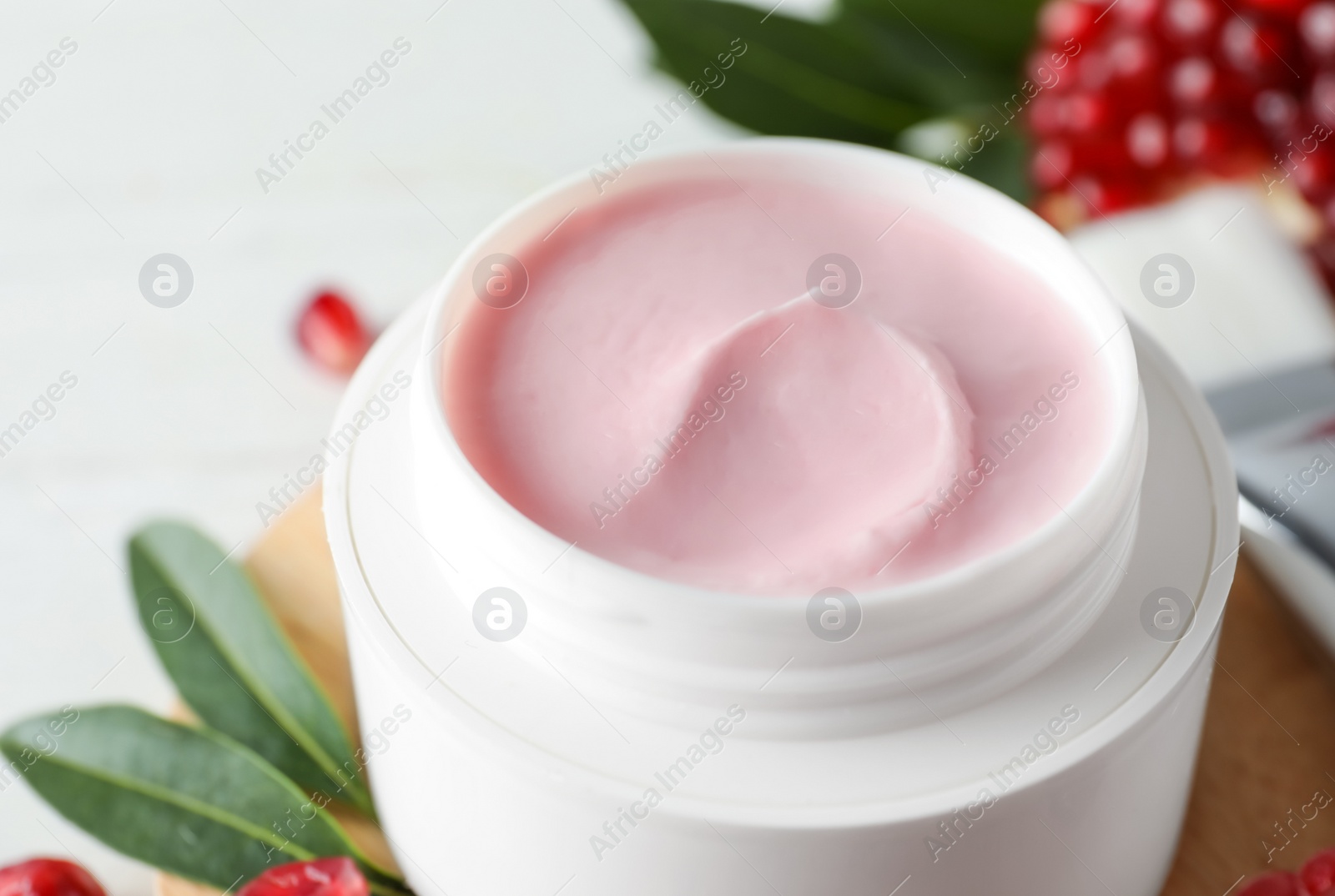 Photo of Jar with natural facial mask, pomegranate seeds and green leaves on table, closeup