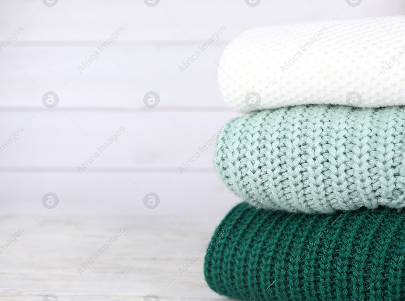 Photo of Stack of soft knitted sweaters on white wooden table. Space for text