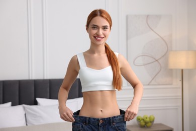 Photo of Slim woman wearing big jeans in room. Weight loss