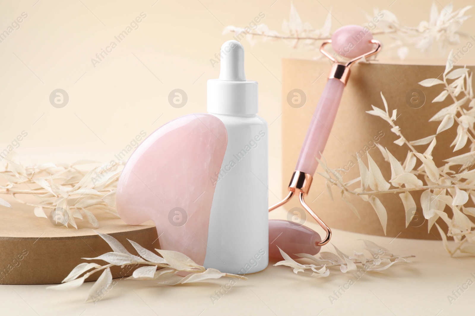 Photo of Composition with rose quartz gua sha tool, facial roller and bottle of serum on beige background