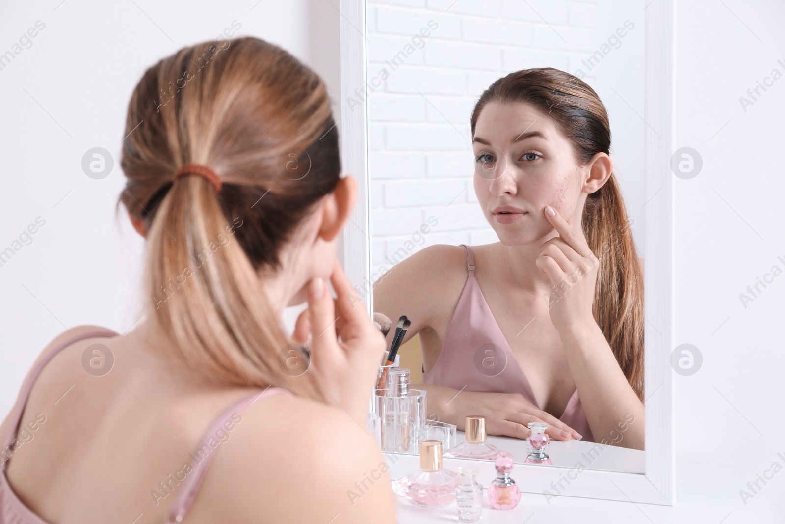 Photo of Woman with acne problem near mirror indoors