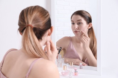 Woman with acne problem near mirror indoors