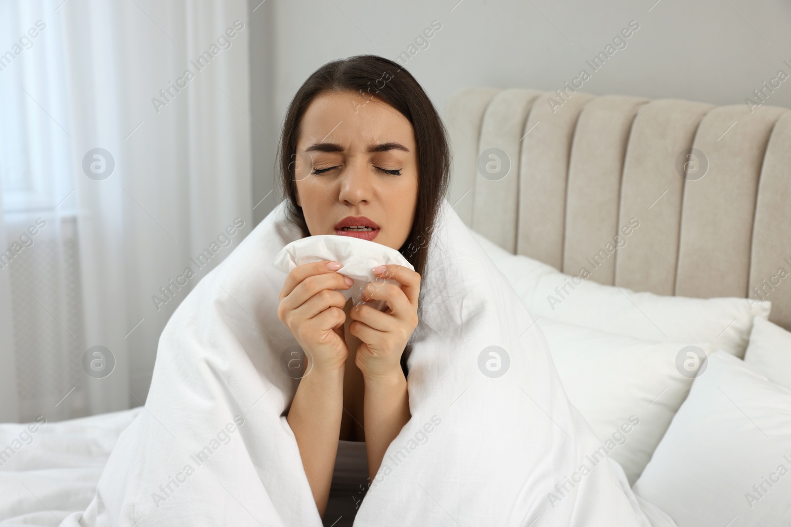 Photo of Sick young woman with tissue wrapped in blanket at home