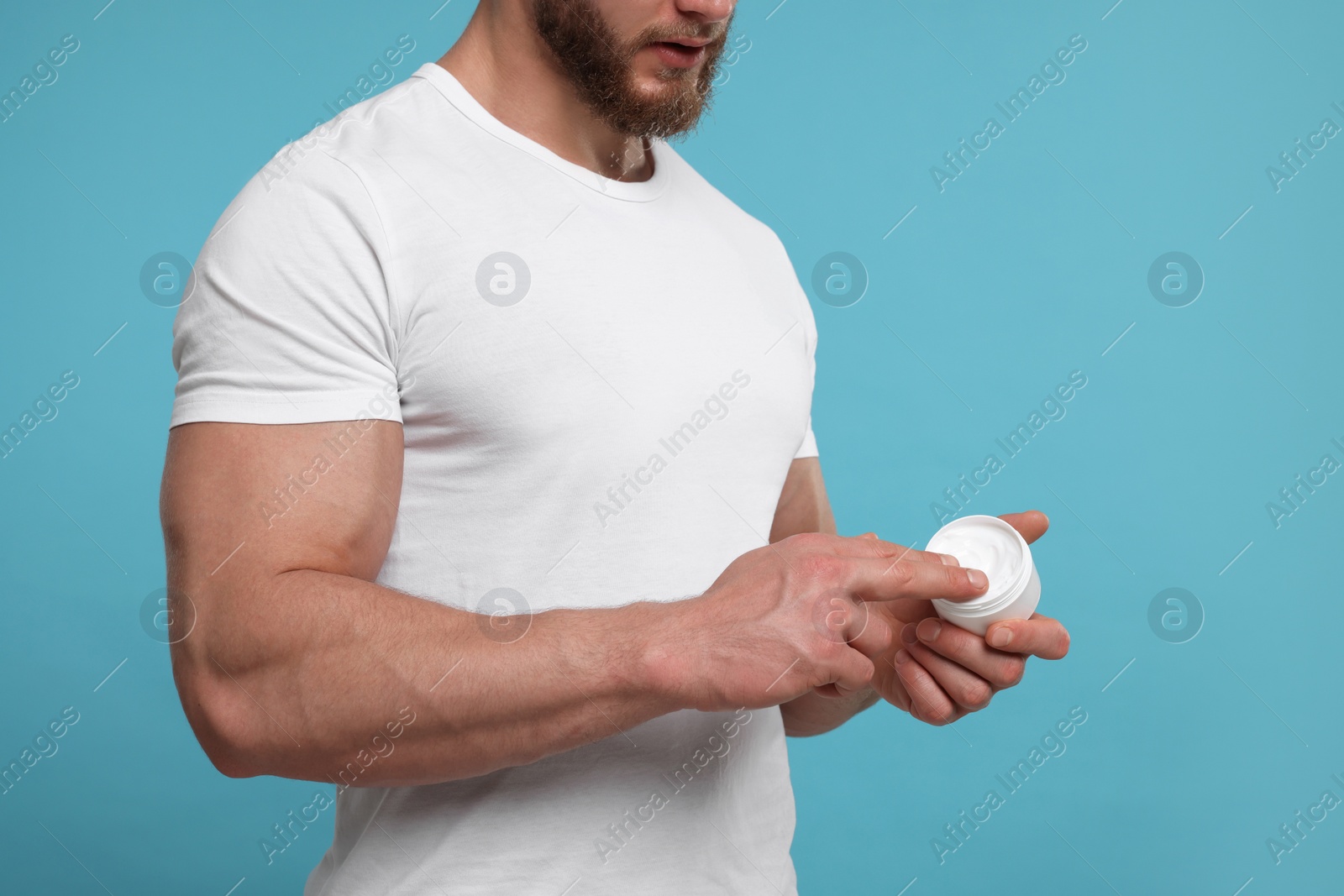 Photo of Man applying body cream on light blue background, closeup