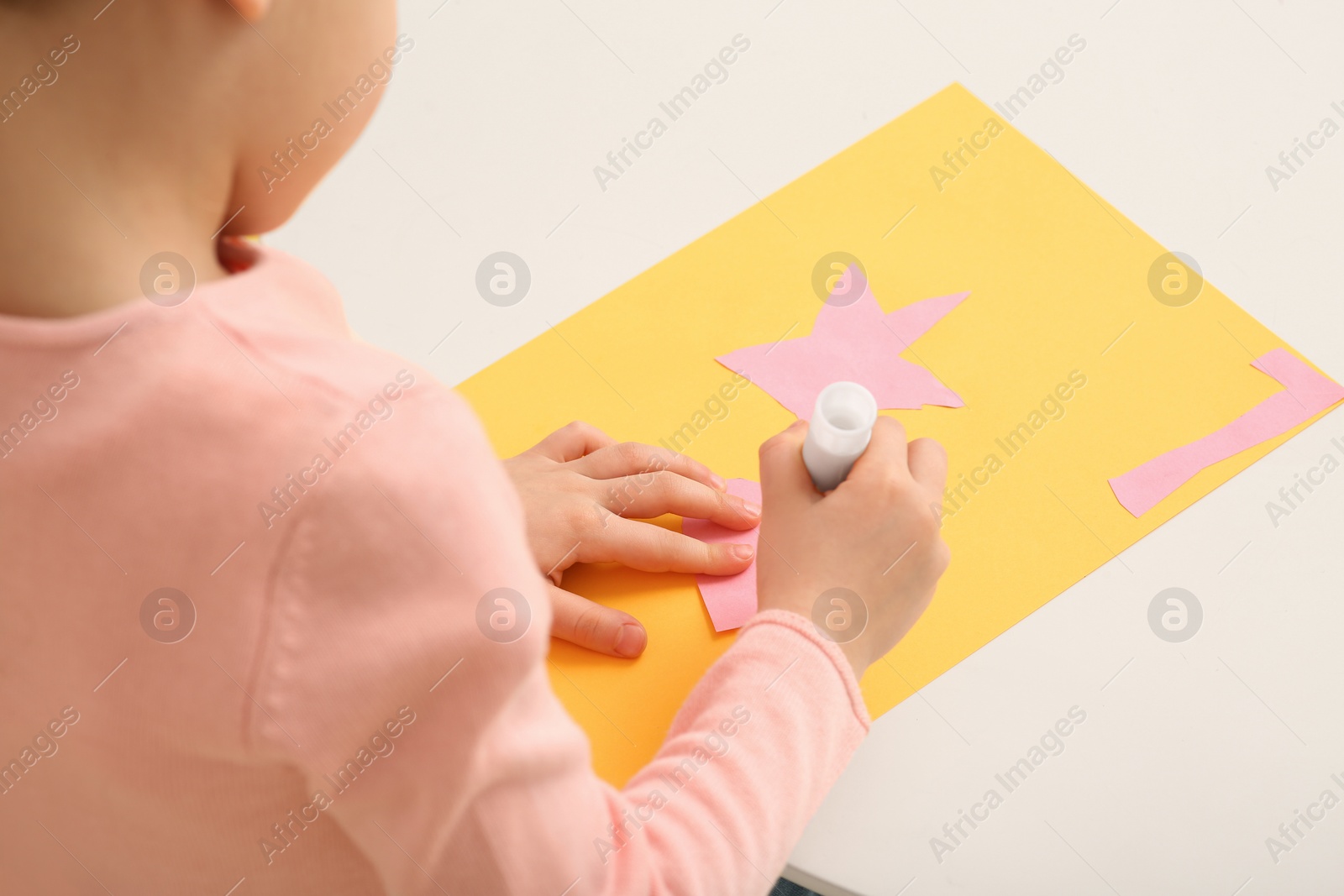 Photo of Girl using glue stick at desk in room, closeup. Home workplace