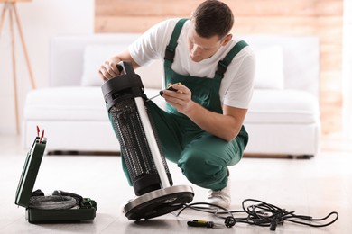 Photo of Professional technician repairing electric patio heater with screwdriver indoors
