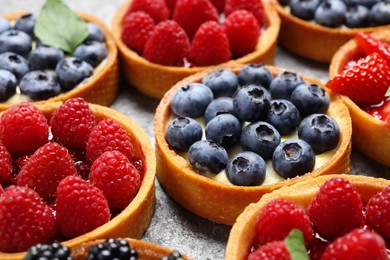 Tartlets with different fresh berries on light grey table, closeup. Delicious dessert