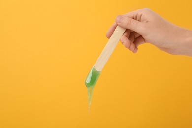 Photo of Woman holding spatula with hot depilatory wax on yellow background, closeup. Space for text