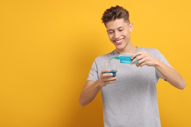 Young man using mouthwash on yellow background, space for text