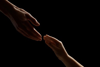 Woman with child on black background, closeup of hands
