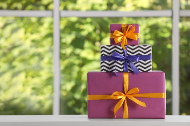 Stack of beautifully wrapped gift boxes on white table  near window. Space for text