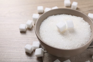 Photo of Different types of white sugar in bowl on wooden table, closeup. Space for text