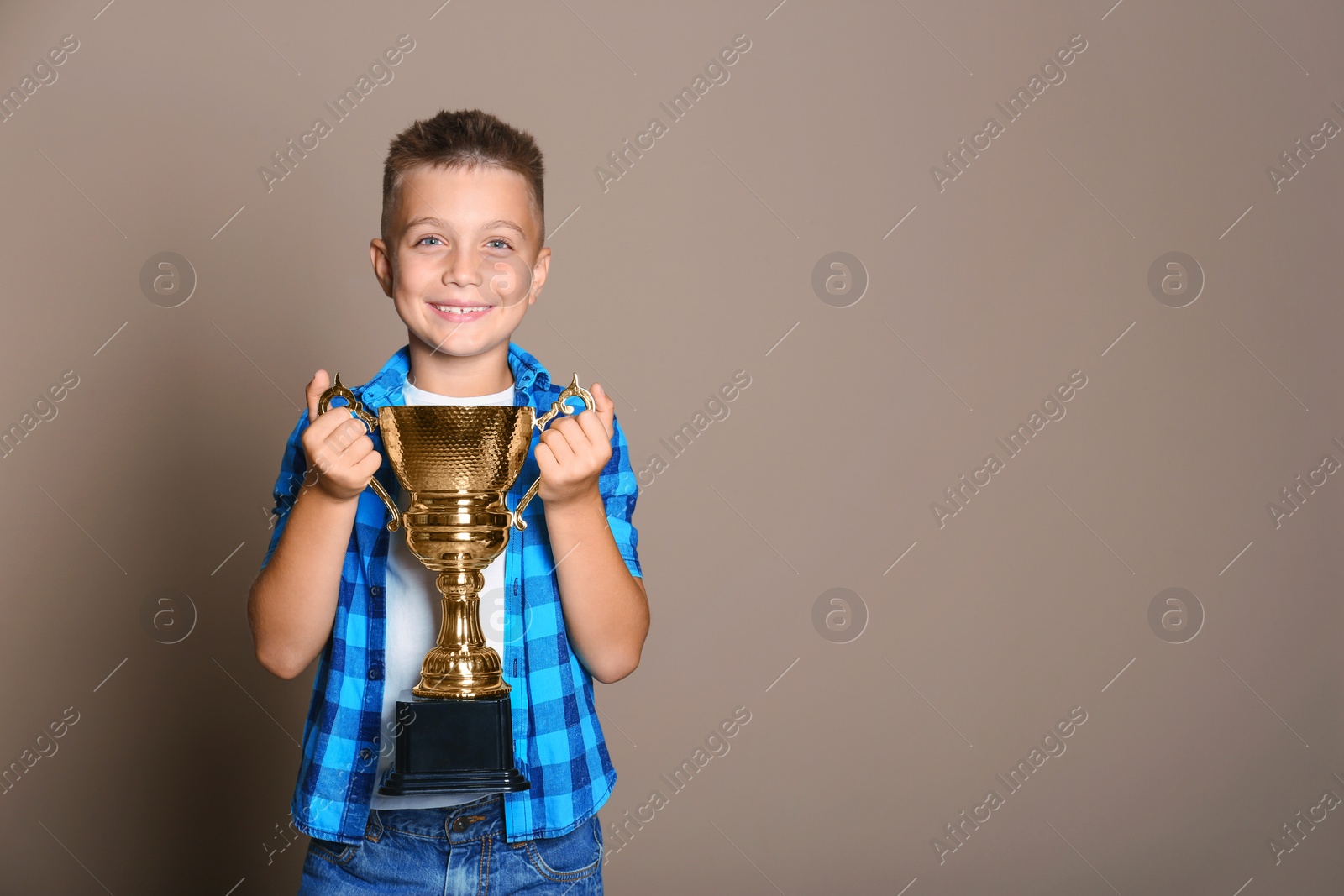 Photo of Happy boy with golden winning cup on beige background. Space for text