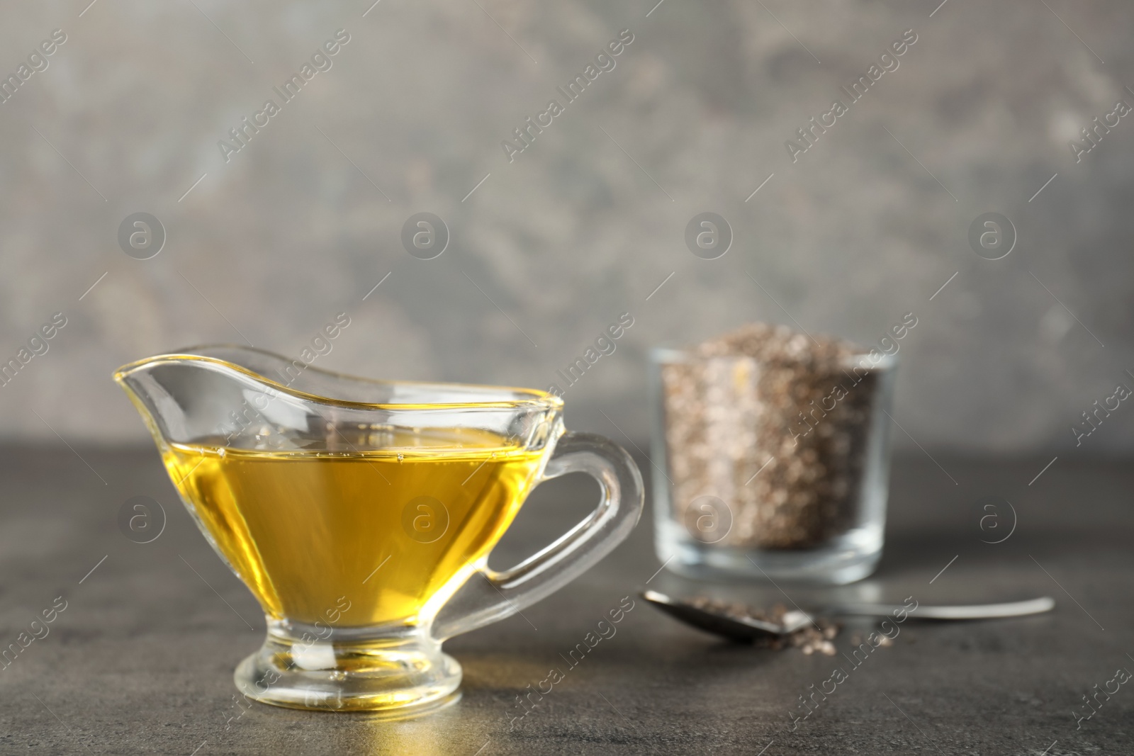 Photo of Sauce boat with chia seeds oil on grey table. Space for text