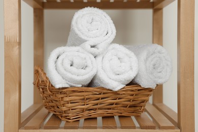 Photo of Soft folded towels in wicker basket on wooden shelving unit
