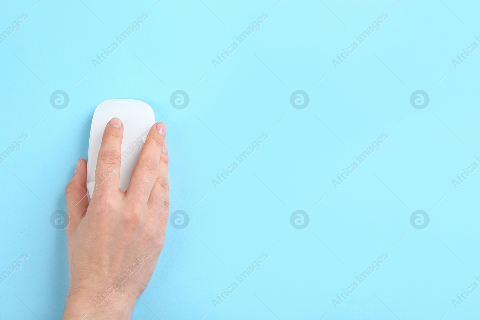 Photo of Woman using modern wireless optical mouse on light blue background, top view. Space for text