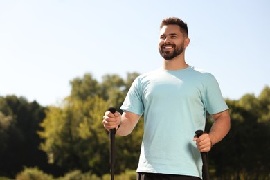 Photo of Happy man practicing Nordic walking with poles outdoors on sunny day