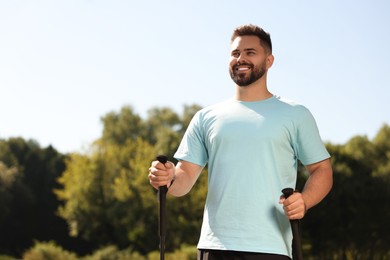 Happy man practicing Nordic walking with poles outdoors on sunny day