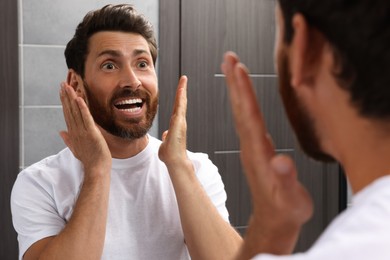 Photo of Emotional bearded man looking at mirror in bathroom